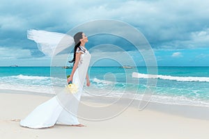 beautiful fiancee in white wedding dress with big long white train and with wedding bouquet stand on shore sea