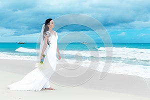 beautiful fiancee in white wedding dress with big long white train and with wedding bouquet stand on shore sea