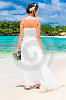 beautiful fiancee in white wedding dress with big long white train and with wedding bouquet stand on shore sea
