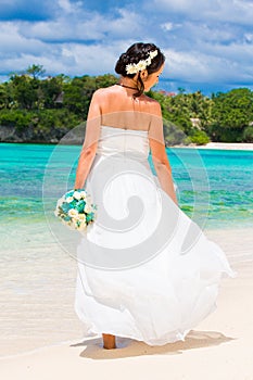 beautiful fiancee in white wedding dress with big long white train and with wedding bouquet stand on shore sea