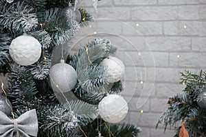 Beautiful fir tree decorated with white baubles and silver bows on brick wall with golden garland lights bokeh. Merry Christmas.