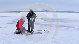 Beautiful fisherwoman in red jacket and felt boots catches fish with help winter fishing rod