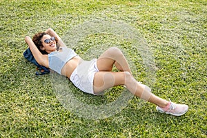 Beautiful fit African-American woman with curly hair happily lying on a lawn at a park