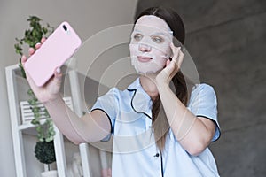 Beautiful fit brunette woman at home in pajama. She do beauty procedures - apply face moisturizing mask and make selfie on her