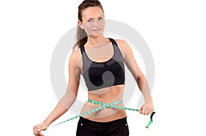 Beautiful fit girl measuring her waist with a green measuring tape in inch.