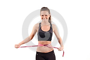 Beautiful fit girl measuring her waist with a pink measuring tape in centimeters.
