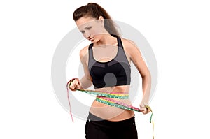 Beautiful fit girl measuring her waist with three measuring tapes looking down.