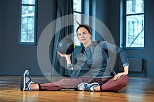 Beautiful fit woman in sportswear posing while sitting on the floor with fitness ball in front of window at gym Healthy