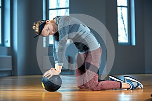 Beautiful fit woman in sportswear posing while sitting on the floor with fitness ball in front of window at gym Healthy