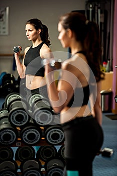 Beautiful fit woman works out with dumbbells in a fitness gym