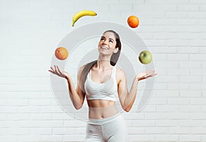 Beautiful, fit, young woman joggling with fruit, over a white brick wall