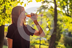 Beautiful fitness athlete woman are drinking iced tea after workout exercising on sunset evening in park.