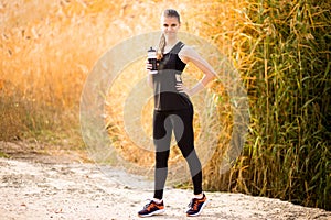 Beautiful fitness athlete woman drinking water after work out exercising on autumn park