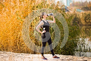 Beautiful fitness athlete woman drinking water after work out exercising on autumn park