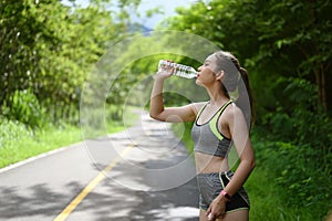 Beautiful fitness athlete woman drinking water after work out exercising outdoor.