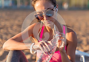 Beautiful fitness athlete woman drinking water after work out exercising on sunset evening summer in beach outdoor