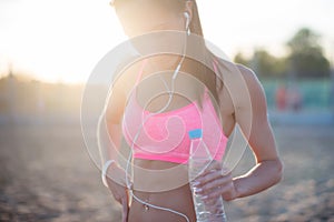 Beautiful fitness athlete woman resting drinking water after work out exercising on beach summer evening in sunny