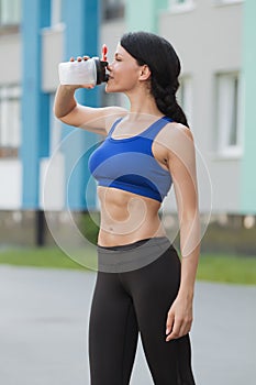 Beautiful fitness athlete woman resting drinking water after work out exercising on beach summer evening in sunny sunshine outdoor