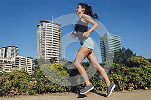 Beautiful fitness girl running in the city with urban background of skyscrapers