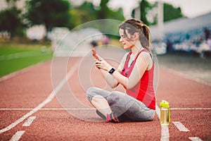 Beautiful fitness girl uses smartphone at stadium after workout. Sports and healthy. Sport woman use of cellphone inside sport