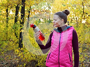 Beautiful fitness sport girl in sportswear with sports water bottle or isotonic drink in hand in autumn forest.