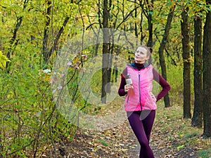 Beautiful fitness sport girl in sportswear with sports water bottle or isotonic drink in hand in autumn forest.