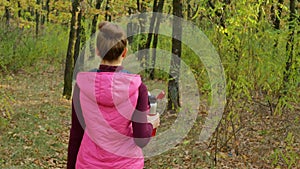Beautiful fitness sport girl walking along the autumn park in sportswear with sports water bottle or isotonic drink in