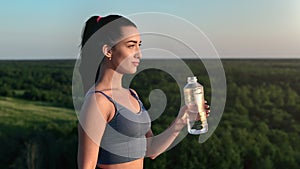 Beautiful fitness woman smiling drinking water bottle on mountain over forest sunset sunrise outdoor