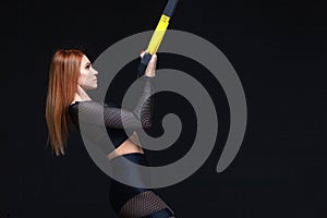 Beautiful fitness woman training with trx fitness straps in sexy sportswear isolated on black background