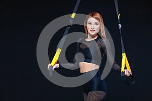 Beautiful fitness woman training with trx fitness straps in sexy sportswear isolated on black background