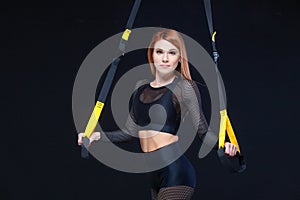 Beautiful fitness woman training with trx fitness straps in sexy sportswear isolated on black background