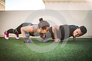 Beautiful fitness young sporty couple doing push ups together at outdoors gym.