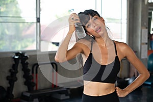 Beautiful fitness young woman tired taking a break from exercise cooling down from water bottle touching her face in gym . healthy