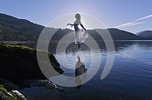 Beautiful Floating Girl dressed in white, silhouetted by the sun reflected in still lake