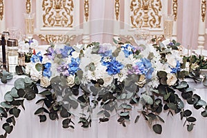 Beautiful floral centerpiece at bride and groom table at wedding reception in luxury restaurant, white and blue flowers on white