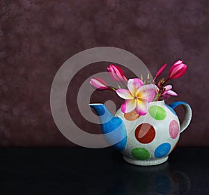 Beautiful flower plumeria or frangipani in fancy baked clay teapot on still life pink dark bokeh background
