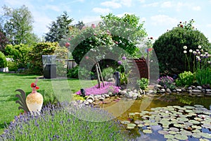 Beautiful flowerbeds with flowering pinks and lavender in garden around pond in summer