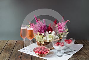 Beautiful flowers, glasses of rose champagne,  italian dessert panna cotta and fresh raspberry on wooden table. Selective focus.