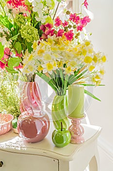 Beautiful flowers in green and pink vases, Candles and glass apples on white wooden  commode. Spring interior decoration