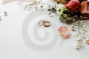 Beautiful  flowers, pearl jewelry and two gold wedding rings on a white background. Marriage concept. Wedding bouquet. Isolated