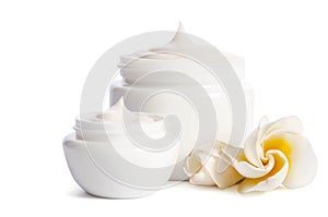 Beautiful flowers and two white jars with natural skincare cream on white background