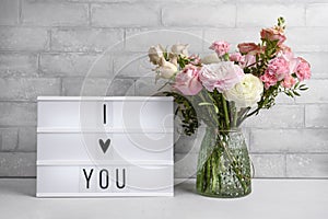 Beautiful flowers in vase and lightbox on a table against grey brick wall. Text i love you. Valentine`s, women`s, mother`s day,