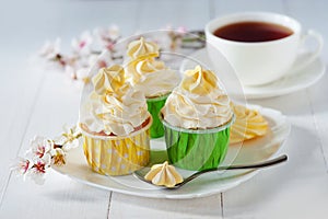 Beautiful flowers on wooden table with white vanilla capcake with meringues and cup of coffee,