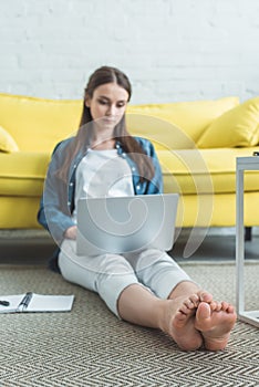 beautiful focused barefoot girl using laptop while sitting on carpet photo