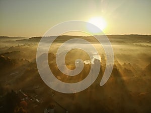 Beautiful foggy forest scene in autumn with orange and yellow foliage. Aerial early morning view of trees and river