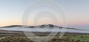 Beautiful foggy sunrise landscape over the tors in Dartmoor revealing peaks through the mist