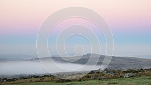 Beautiful foggy sunrise landscape over the tors in Dartmoor revealing peaks through the mist