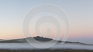 Beautiful foggy sunrise landscape over the tors in Dartmoor revealing peaks through the mist