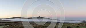 Beautiful foggy sunrise landscape over the tors in Dartmoor revealing peaks through the mist