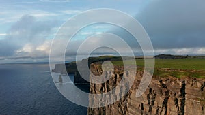 Beautiful footage of sea coast with high rocky cliffs at sunset. Fly around tip of rock edge. Cliffs of Moher, Ireland